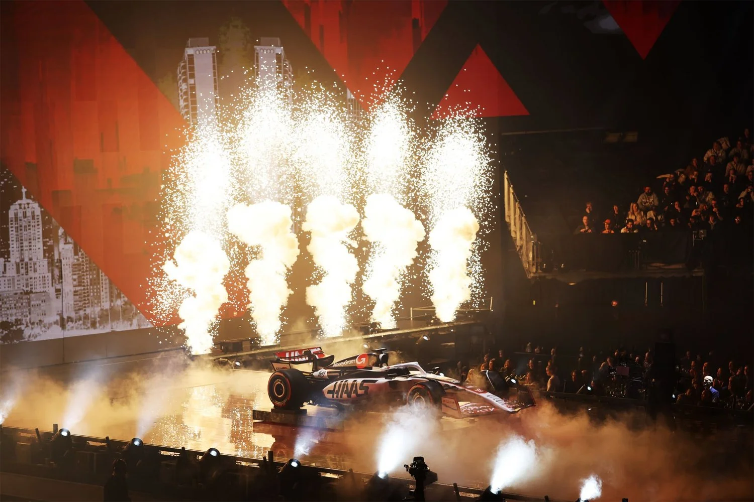 A Formula 1 race car on a stage with fireworks and smoke, surrounded by an audience, during a celebration or event.
