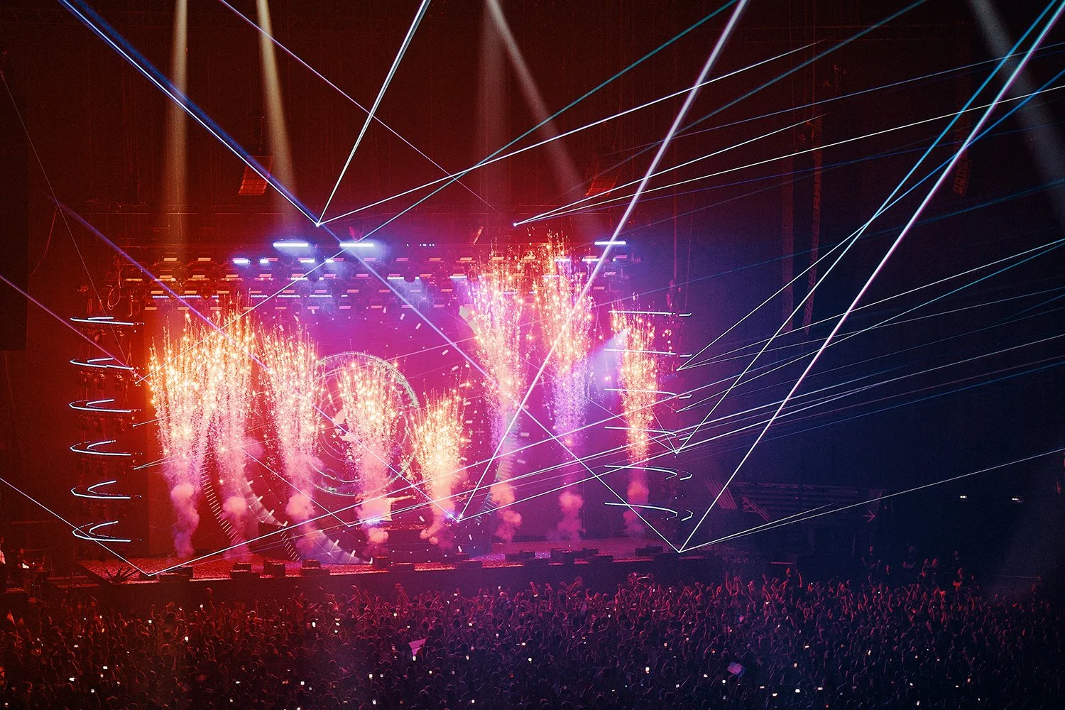 A concert stage with bright fireworks, laser light displays, and a large audience.