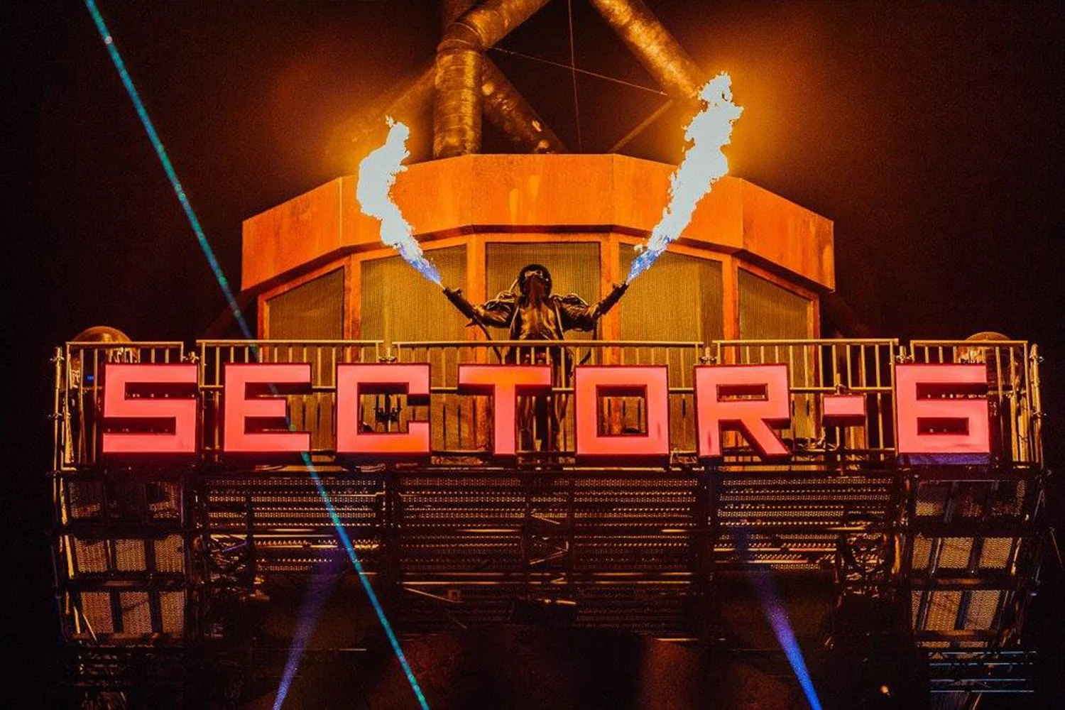 A person in a black jacket and goggles is standing on a balcony at night, holding two torches with flames, above a large illuminated sign that says 'SECTOR 6'. Large industrial pipes are visible above and behind the person, and colored lights are shining across the scene.