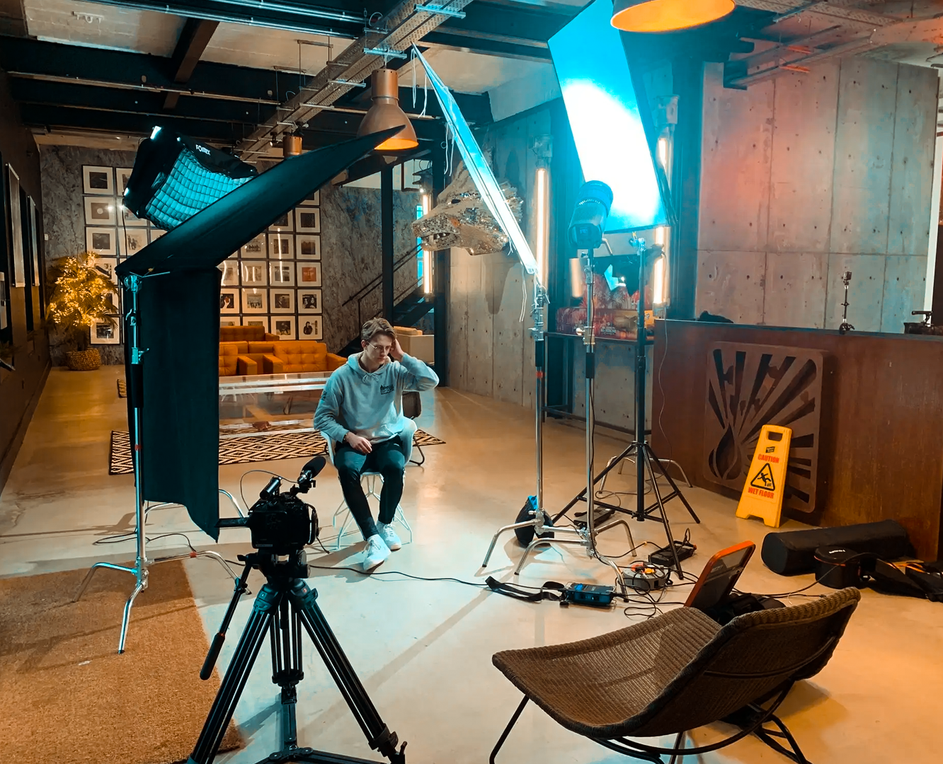 A person sitting in a chair in front of a camera setup and professional lighting, preparing for a video or photo shoot in an indoor studio with modern decor.