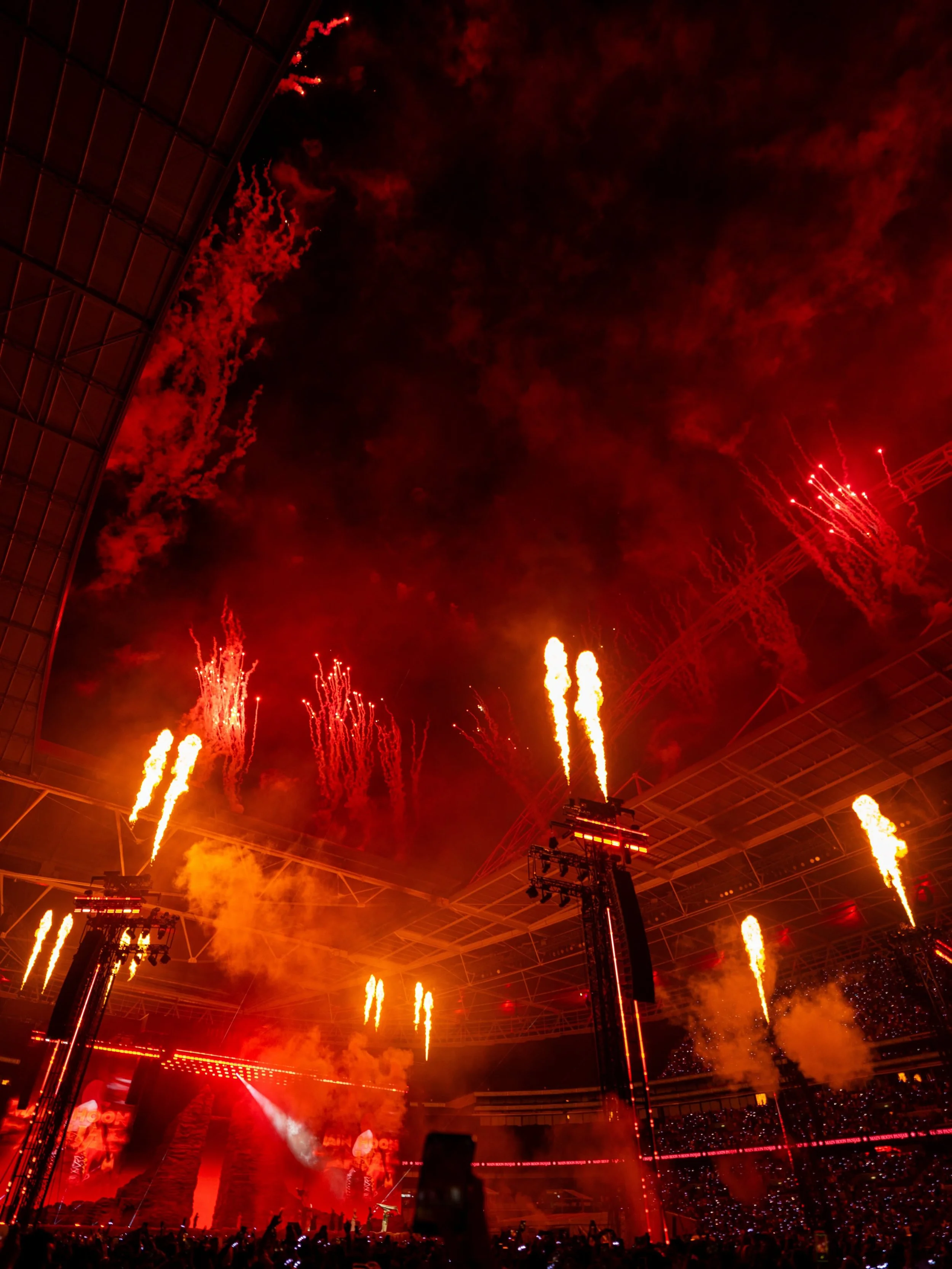 A stadium at night illuminated by fireworks and bright red lights during a concert or celebration.