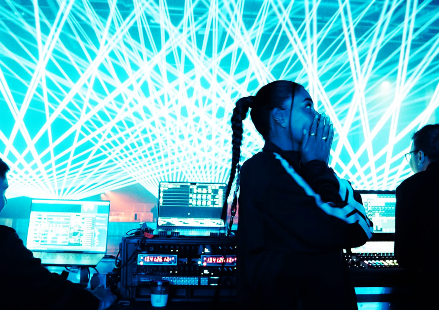 People working at a DJ or music production setup with a vibrant digital light display in the background.