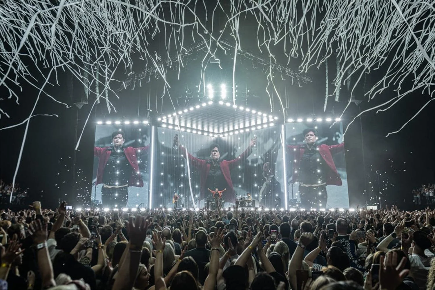 A concert with a large crowd and a performer on stage with big LED screens and bright lights.