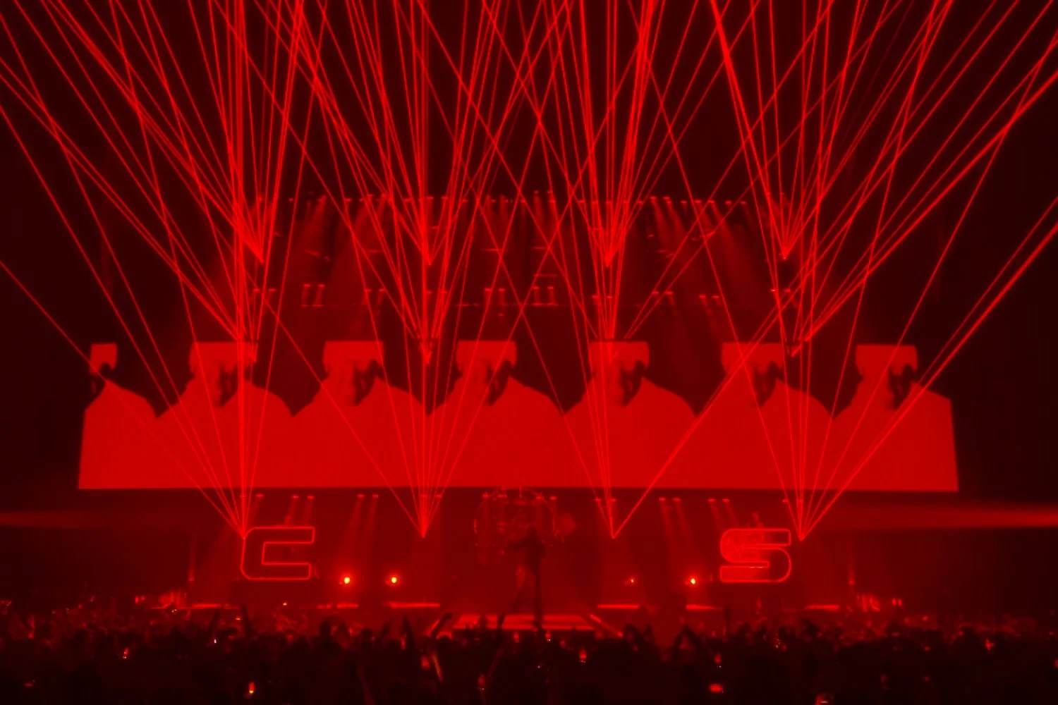 Red laser lights display on a stage, with a large screen showing silhouette images of a dancer. The stage has large neon letters "C" and "S" at the front.