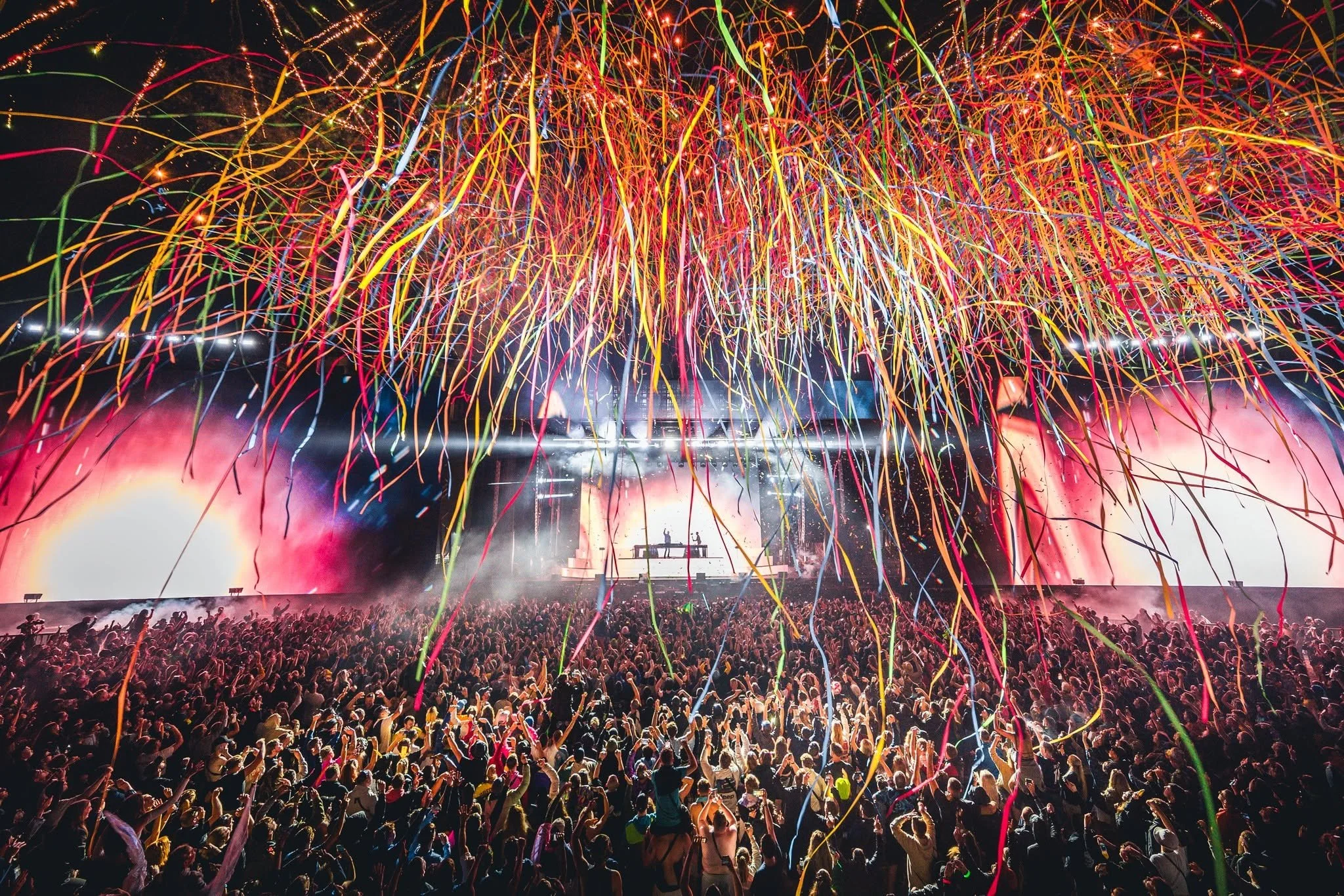 Crowd watching a fireworks display with colorful streamers and pyrotechnics lighting up the sky at night.