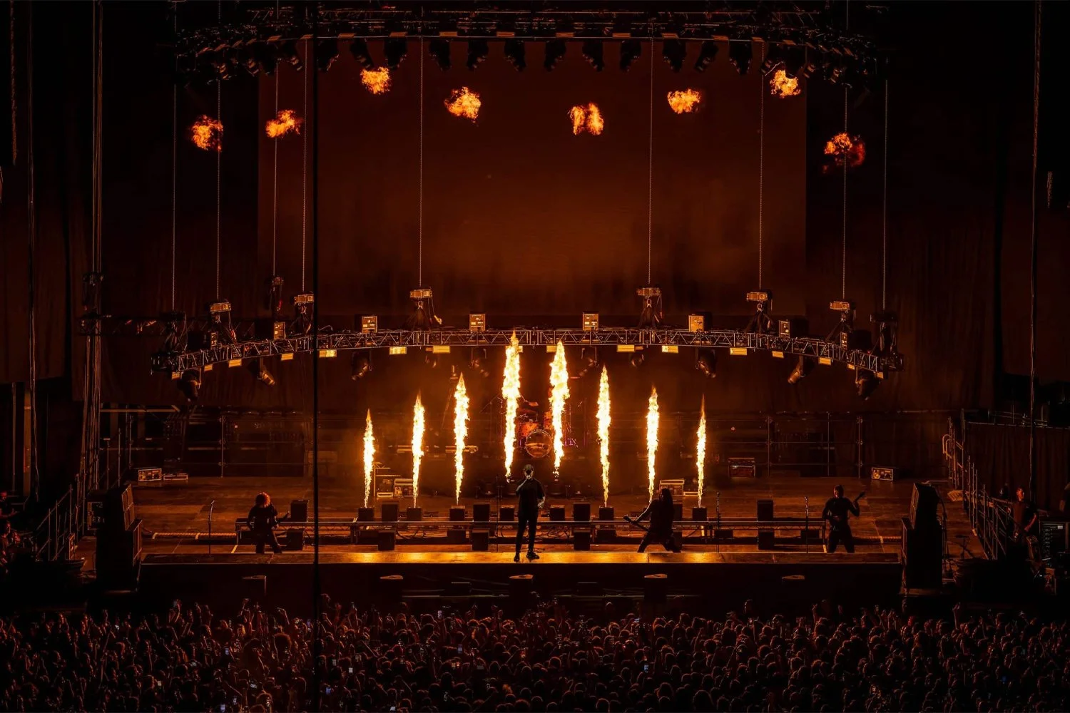 A concert stage with pyrotechnics, flames rising from the floor, and a band performing in front of a large audience.