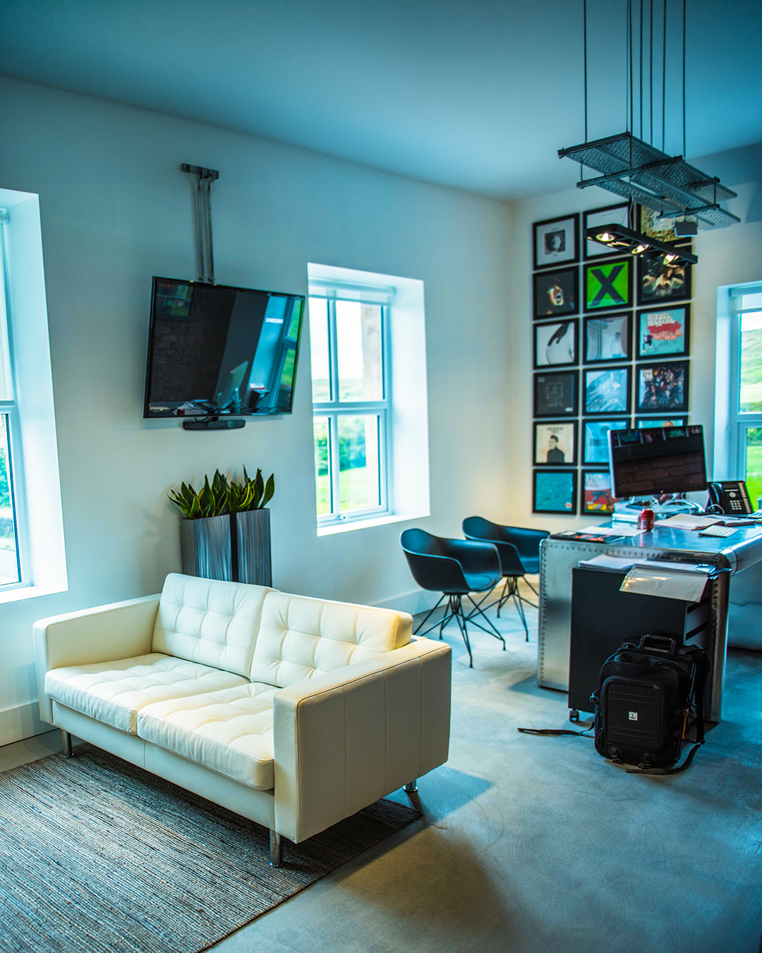 Modern office or studio space with white tufted sofa, black chairs, computer desk, wall art, TV, and large windows letting in natural light.