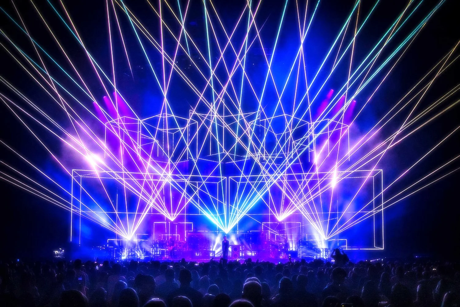 A concert stage with vibrant purple and blue laser light show, with an audience in front and a performer on stage.