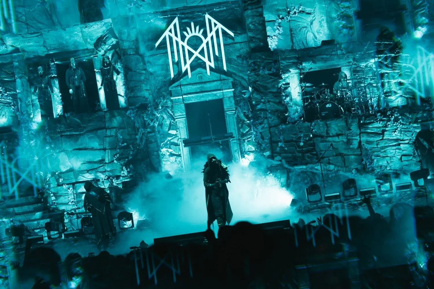 A concert stage with blue lighting, fog effects, and gothic architecture. A performer stands at the center, with band members and musical instruments visible in the background.