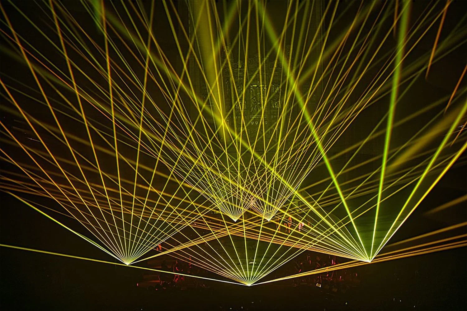 Yellow laser lights crisscross in a dark concert or event space, creating a vibrant light show.
