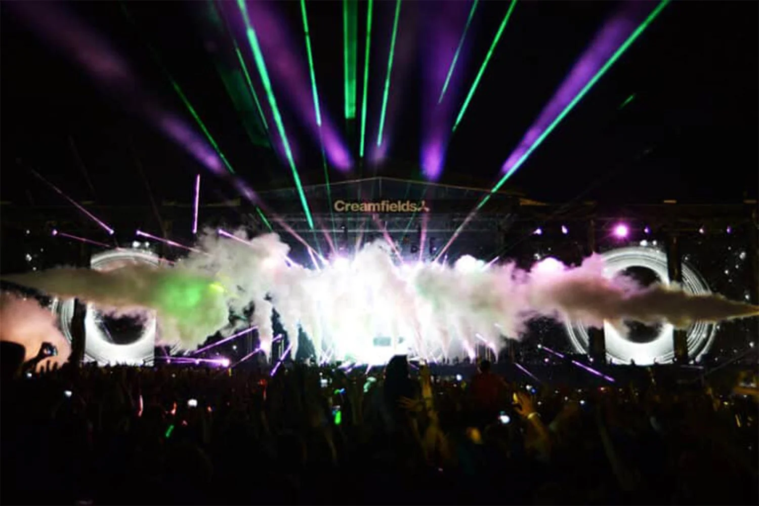 Concert stage with colorful laser lights, smoke effects, and an audience in front, at a festival called Creamfields.