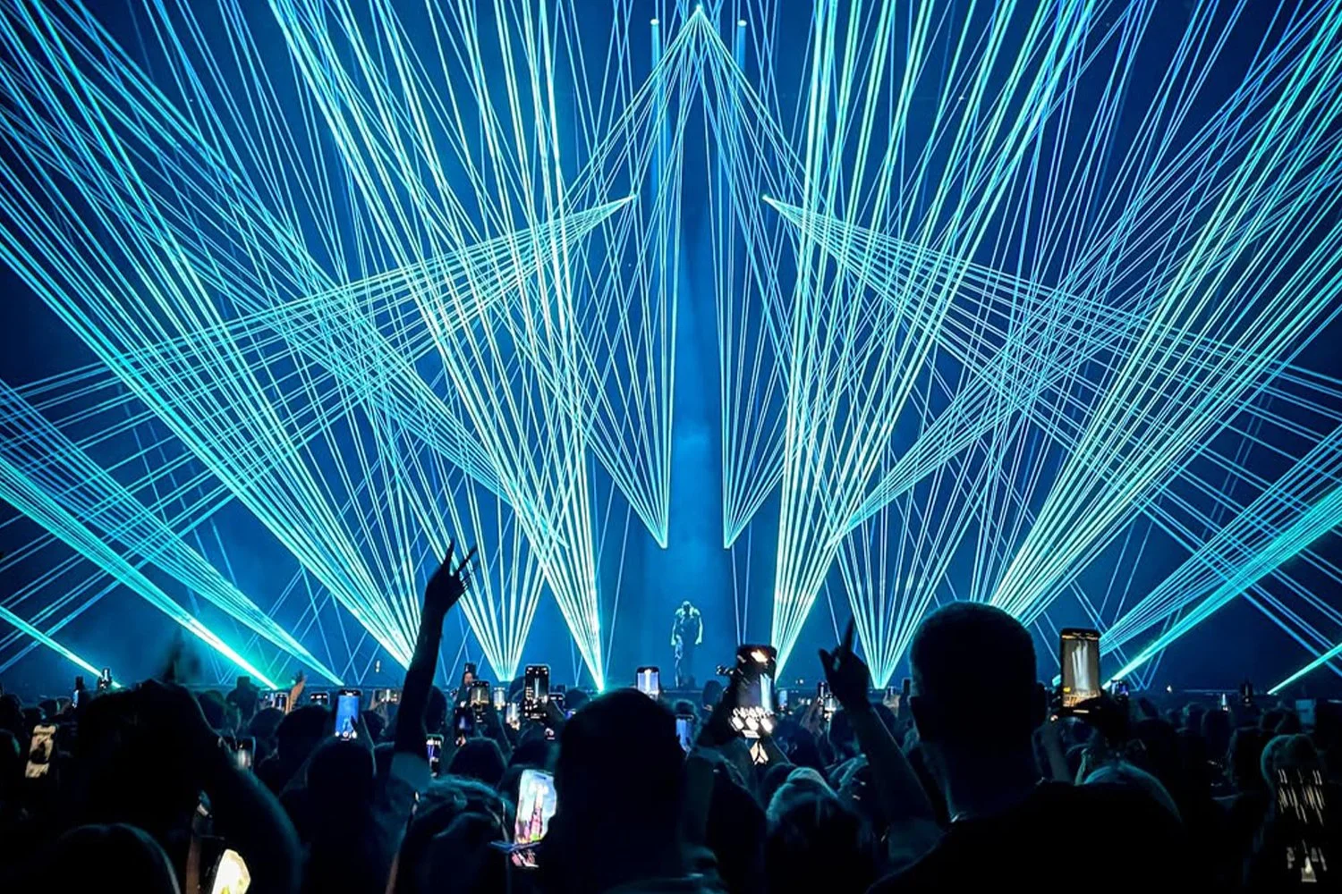 Crowd of people at concert or event with laser light show in the background.