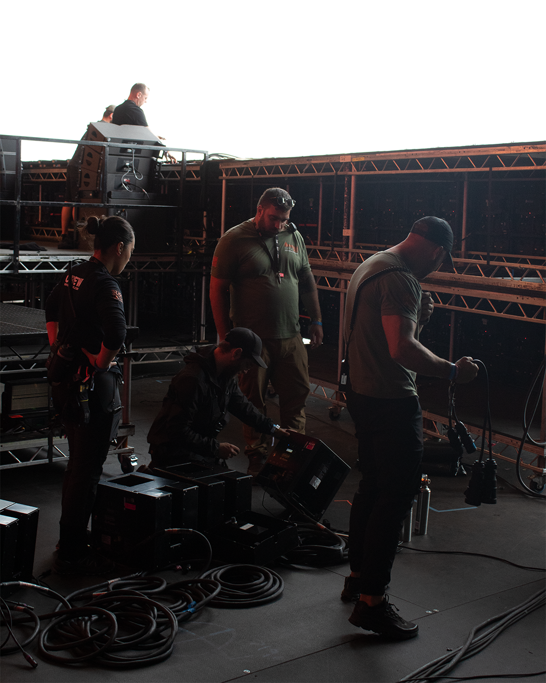 Group of technicians setting up equipment on a stage with scaffolding and cables in a concert or event venue.