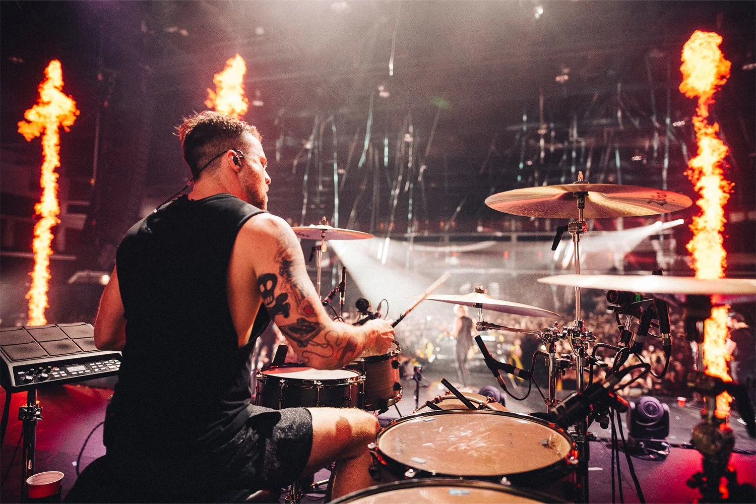 Drummer performing on stage with flames and concert lighting in the background during a live music event.