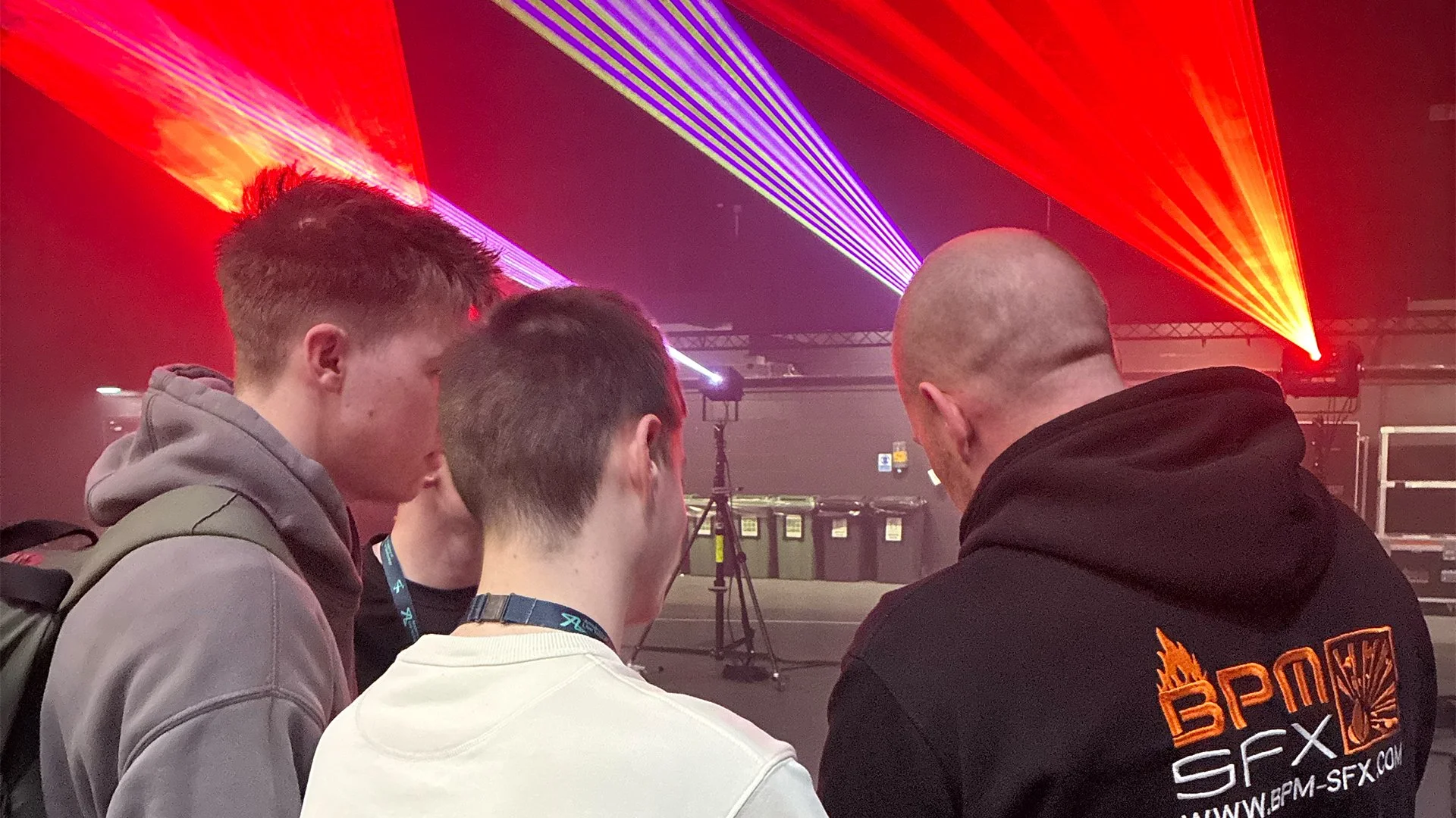 Four young men are standing together at an event with colorful laser lights in the background.