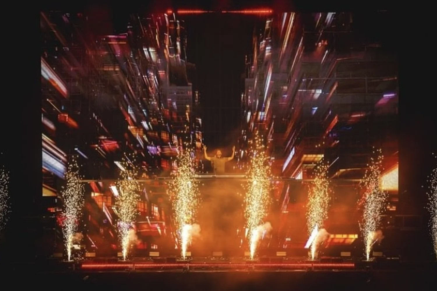 A robot sculpture with arms raised, surrounded by bright fireworks and digital cityscape projections.