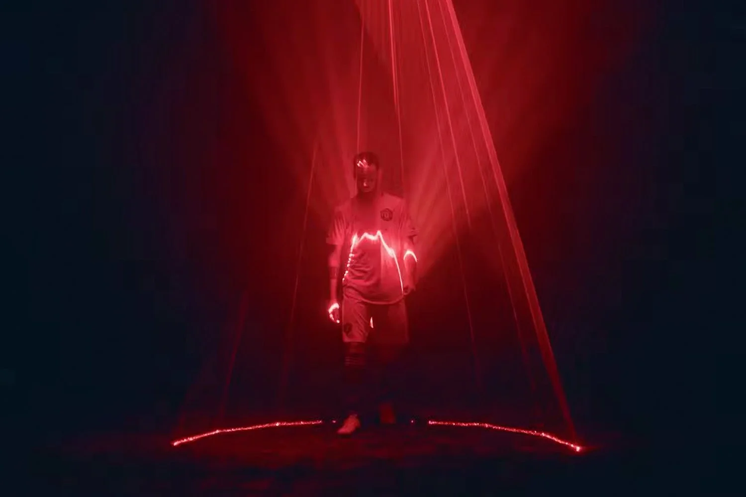 A man in a sports jersey stands in a dark room illuminated by red laser lights forming a geometric pattern around him.