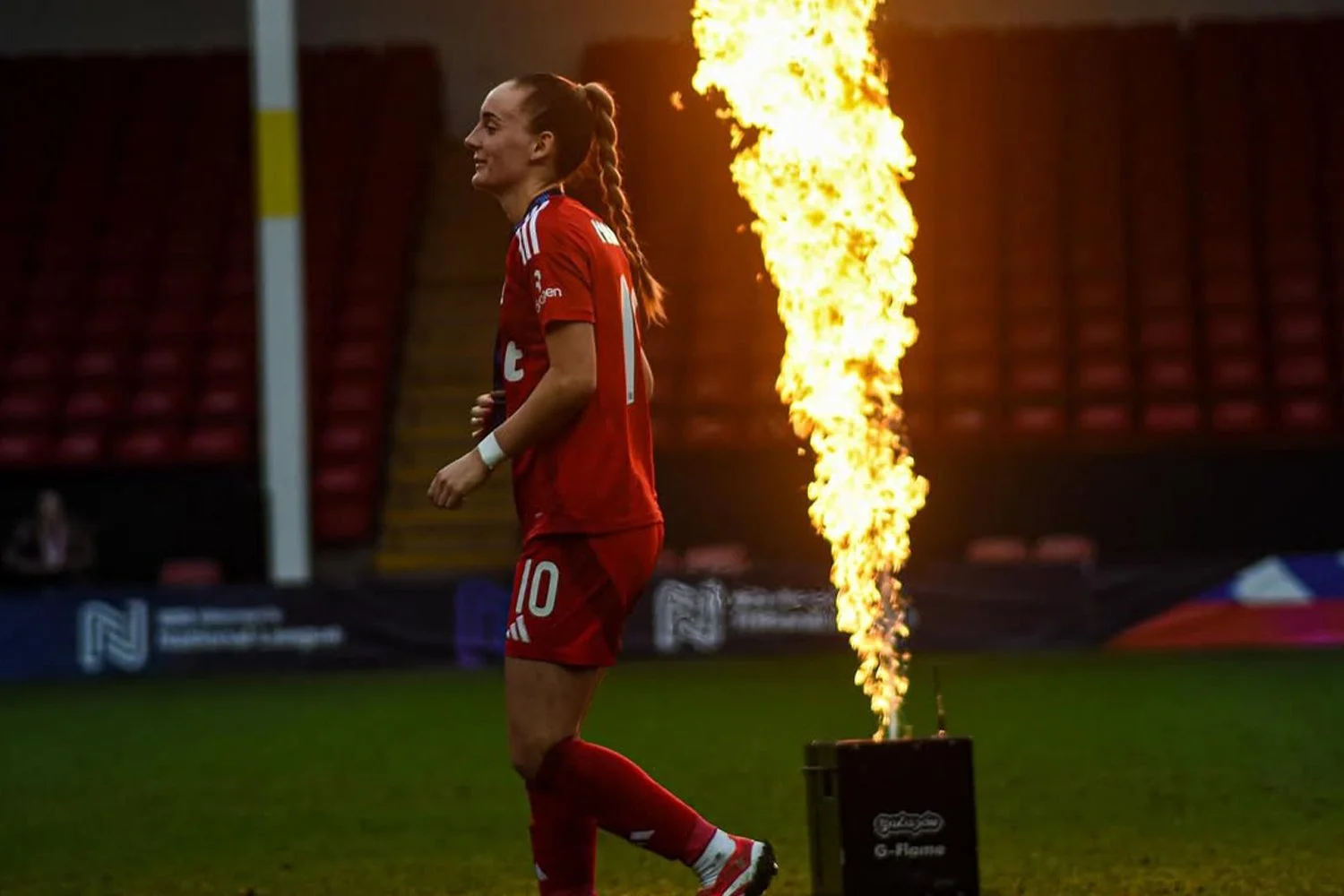A female soccer player in a red uniform with the number 10 on her shorts running on the field during a game, with a large fire effect behind her.