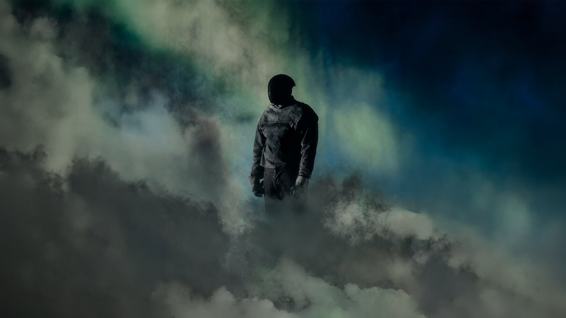 A person wearing a helmet and jacket standing amidst dark clouds and fog, with a mysterious and moody atmosphere.