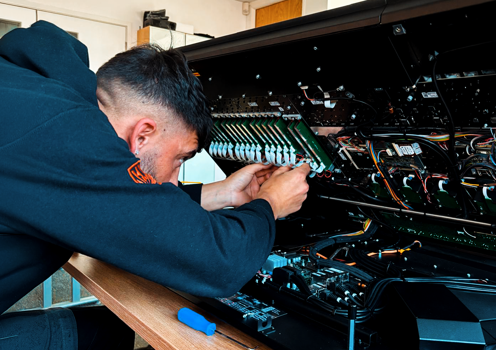 Man working on the inside of a large black electronic device, possibly a cryptocurrency mining rig, with various wires and circuit boards visible.