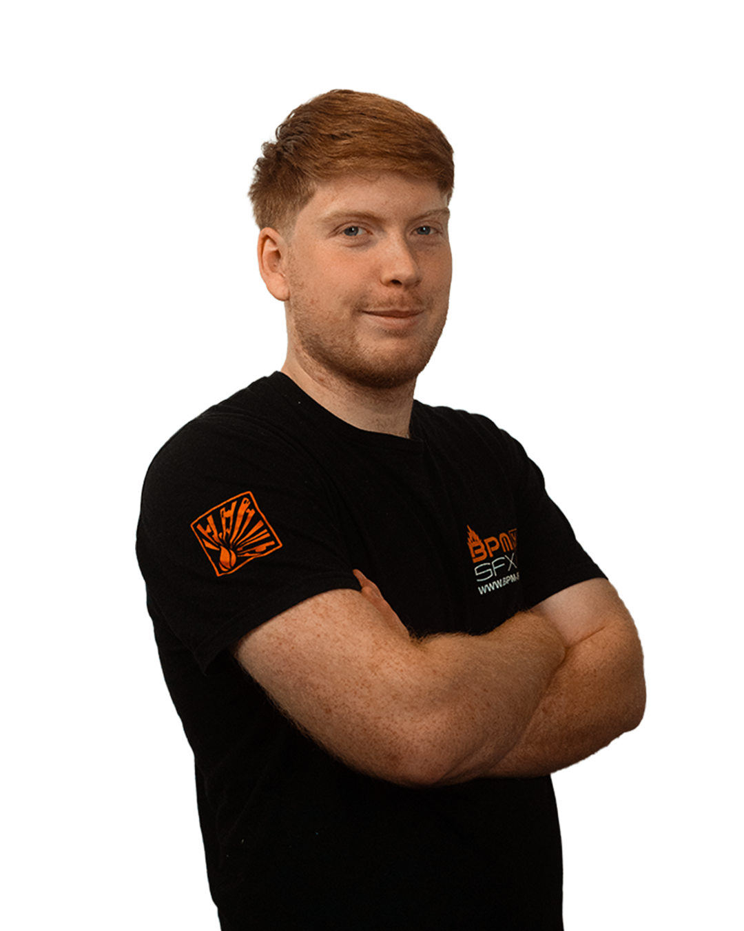A young man with short red hair and a beard, wearing a black T-shirt with orange logos, standing with arms crossed and smiling.