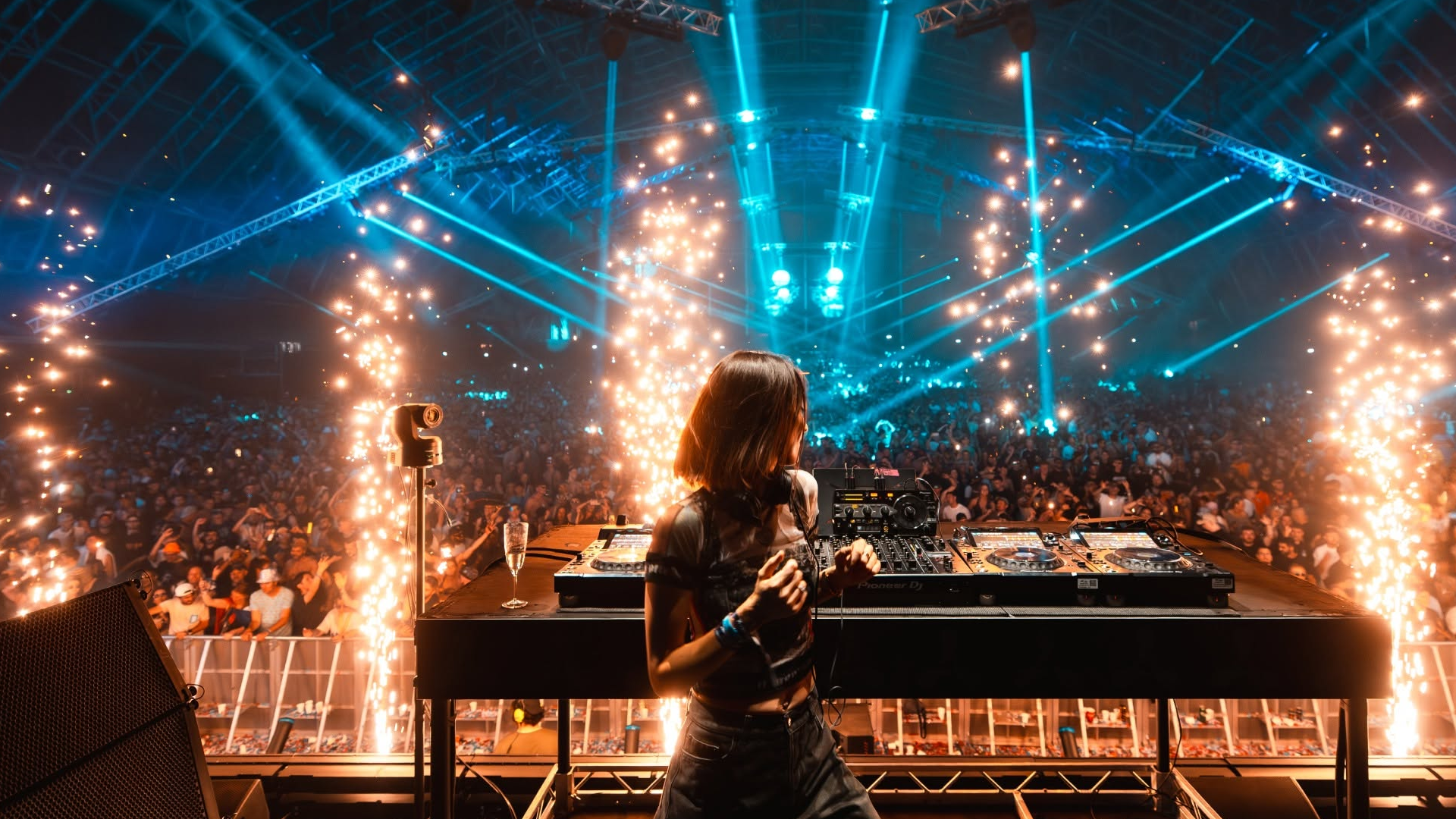 A DJ performing at a concert with a huge crowd, colorful lights, and pyrotechnics.