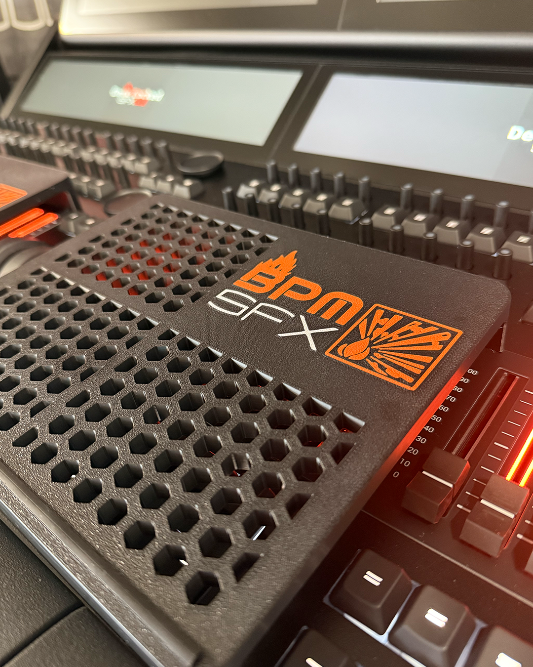 Close-up of a DJ controller with a black and orange BPM and SFx sticker, and illuminated volume sliders.