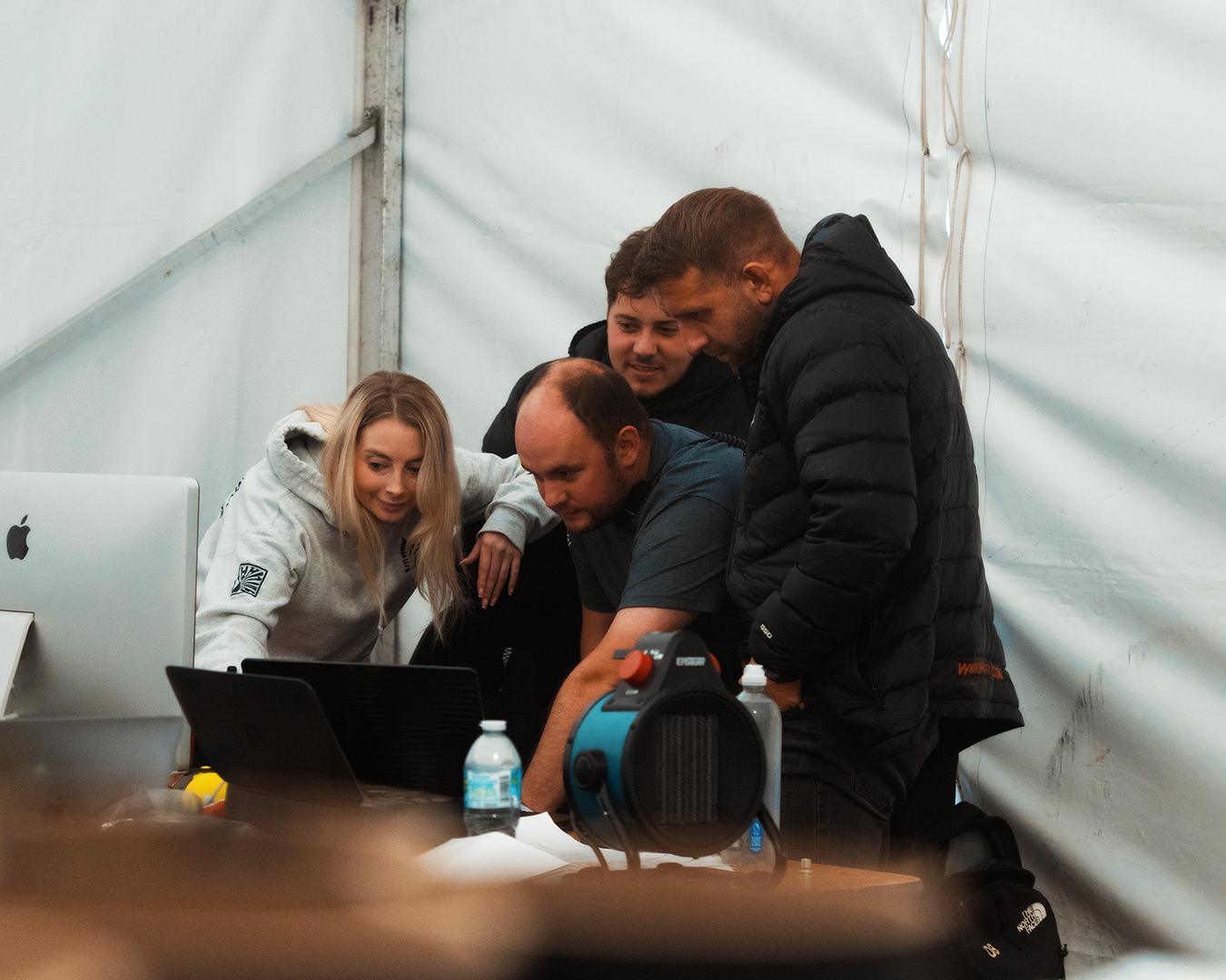 Four young adults gathered around a computer and looking at the screen inside a white tent.
