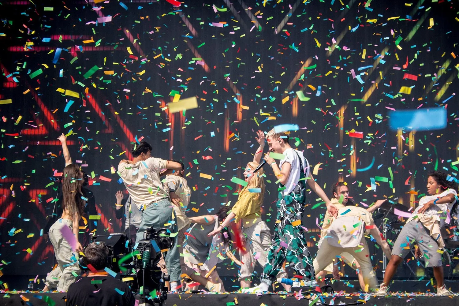 Group of people performing on stage with colorful confetti falling around them.
