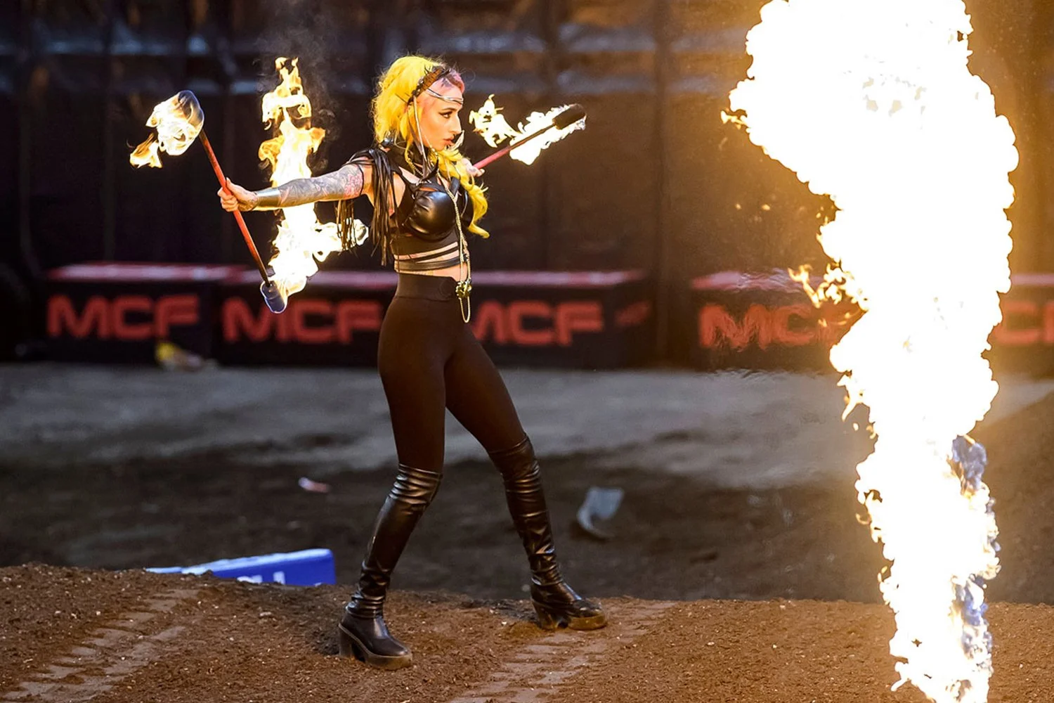 A woman in black leather outfit performing with fire poi, with flames shooting from the fire in front of her