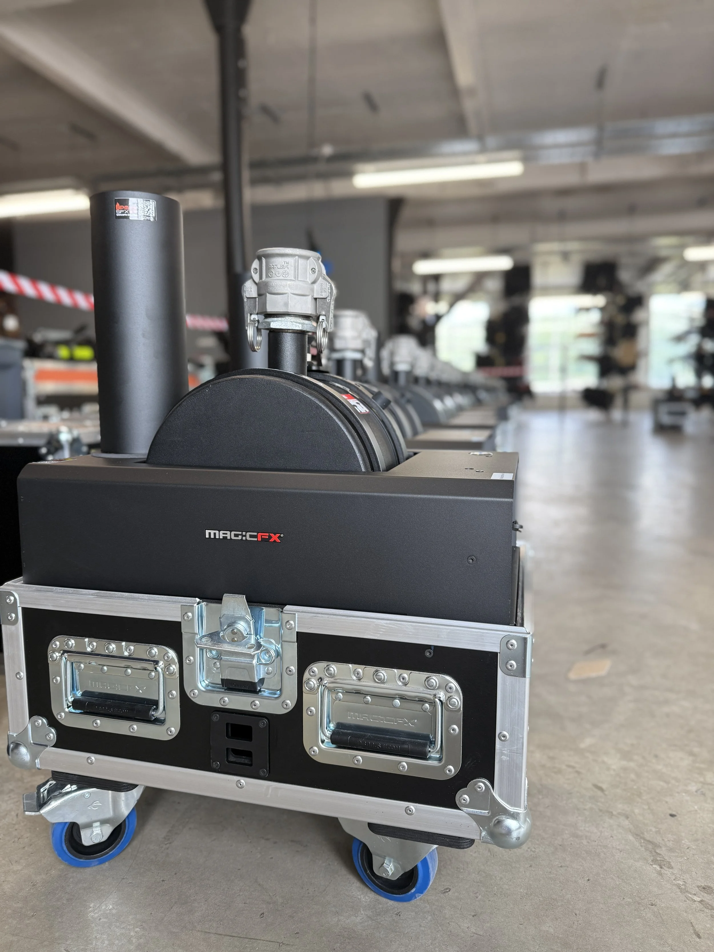 A piece of flight simulation equipment, labeled MAC: CFX, mounted on a wheeled metal cart with blue and black wheels, set in an industrial-looking room with a concrete floor and ceiling lights.
