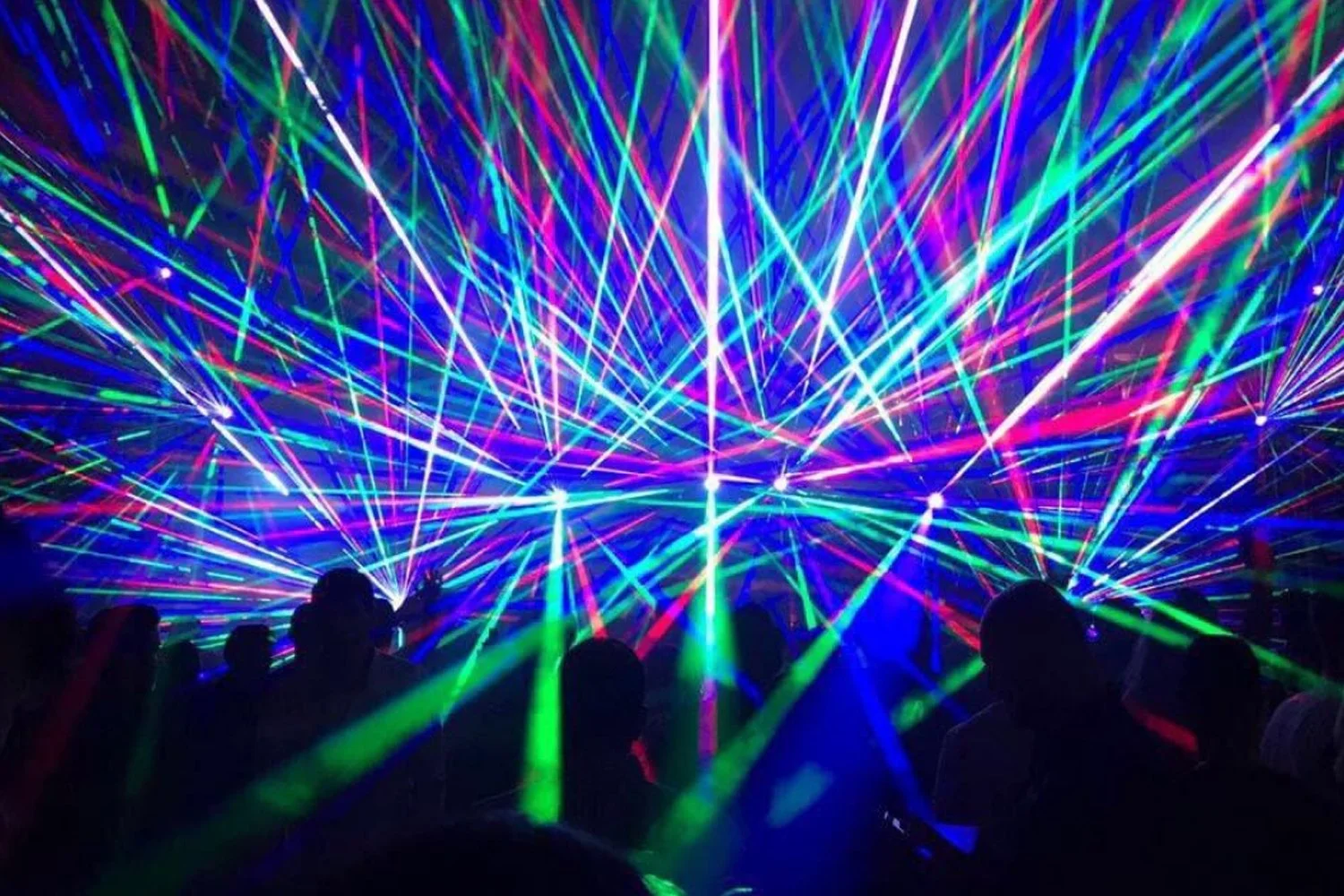 Crowd watching a laser light show with colorful beams of light crisscrossing in various directions.