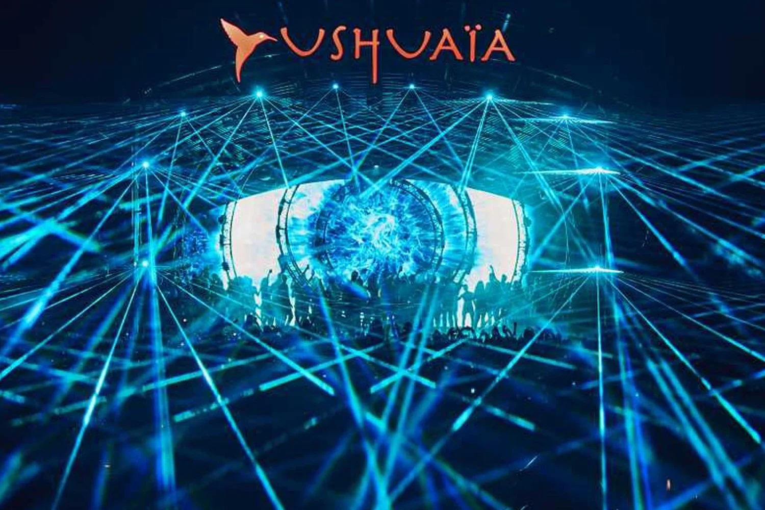 A concert stage with blue laser lights and silhouettes of people dancing, with a large digital display showing an abstract blue design, and the word 'Ushuaïa' displayed above.