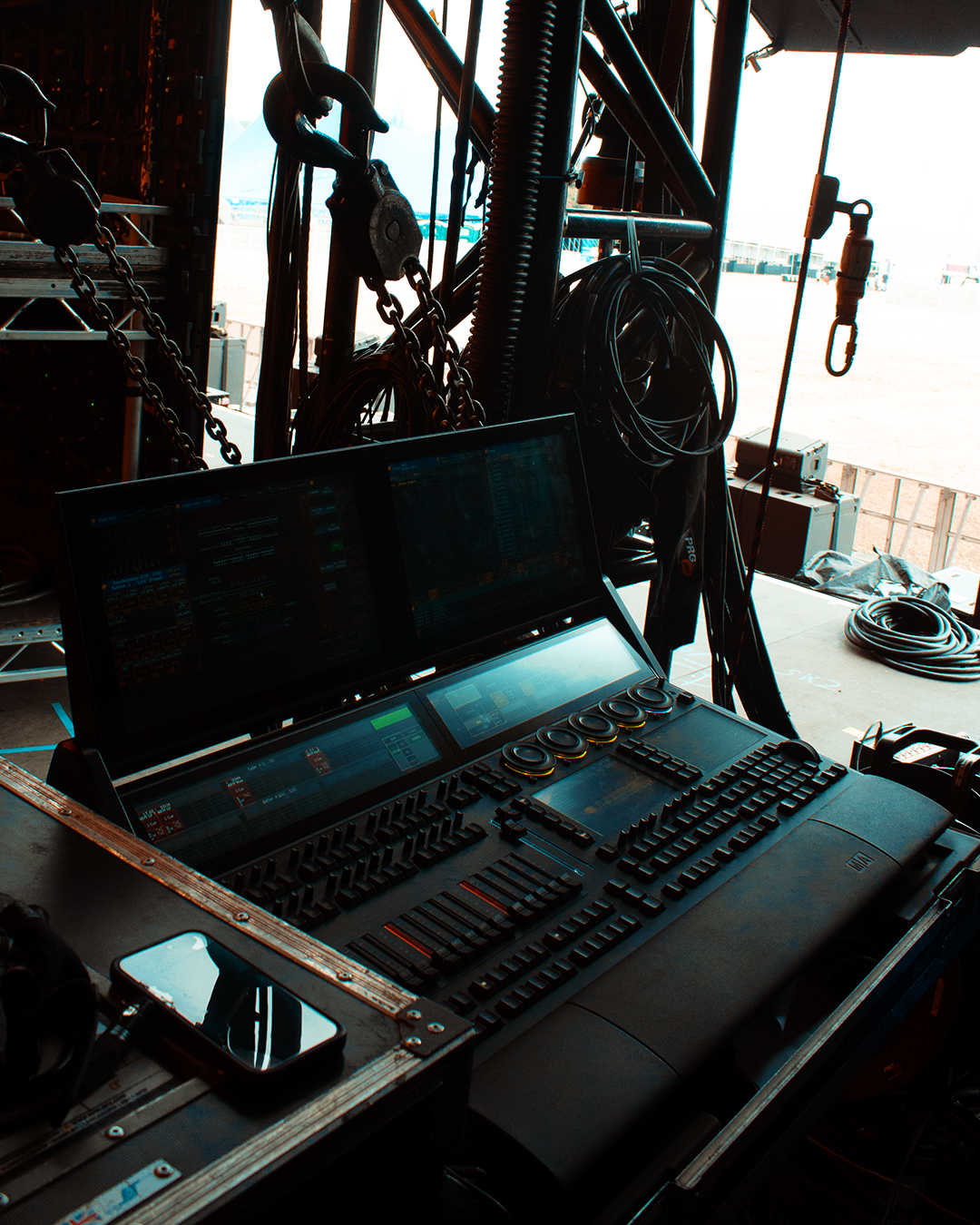 DJ or sound mixing console with two large screens, various controls, and equipment cables, set in a tent at an outdoor event venue.