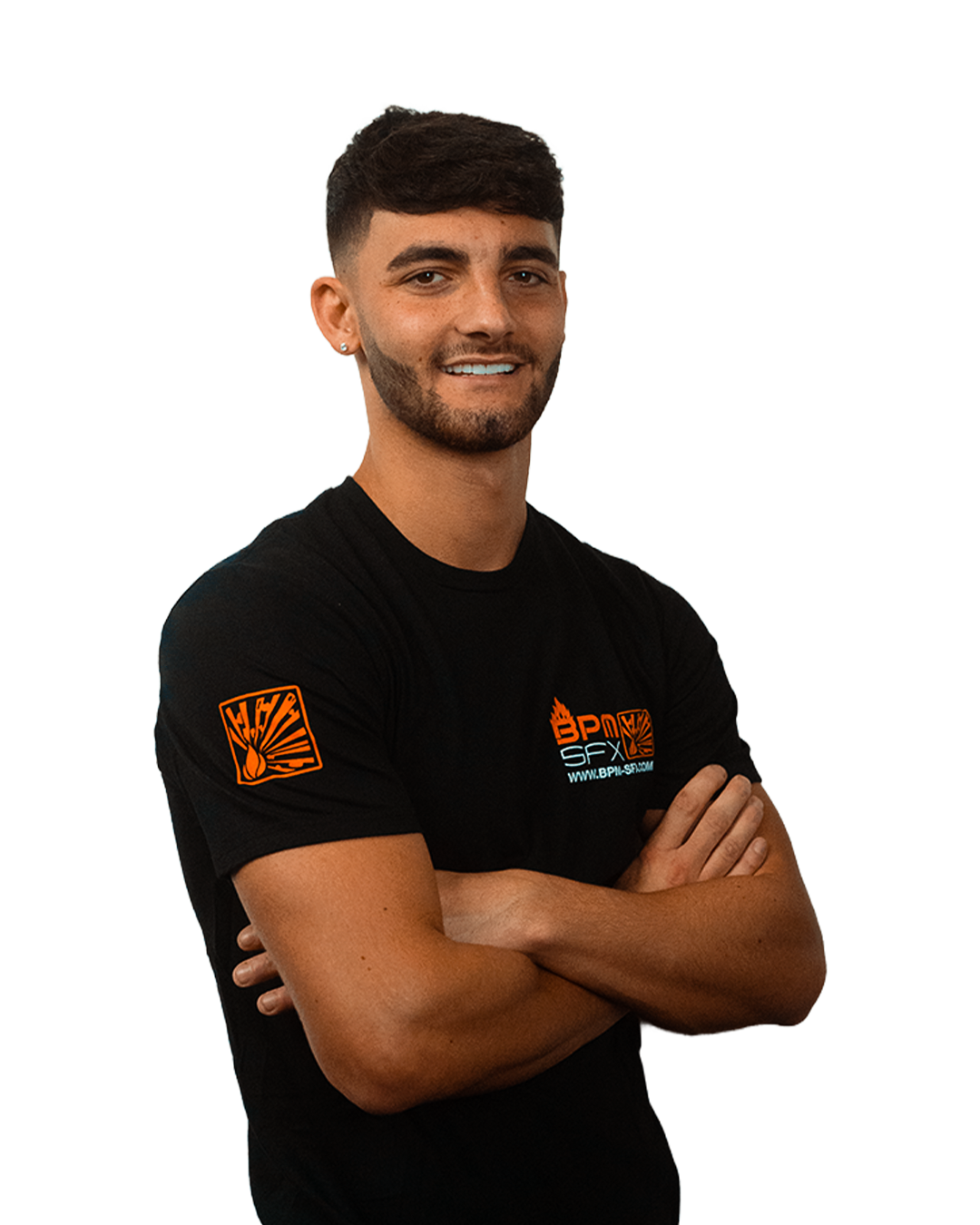 A young man with dark hair and a beard, smiling and crossing his arms, wearing a black t-shirt with orange graphics and text, standing against a plain background.