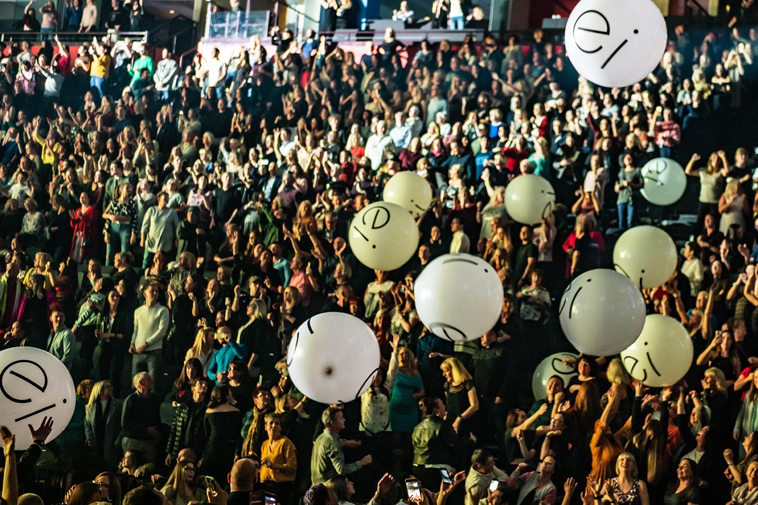 Crowd of people at a large indoor event with white balloons in the foreground.