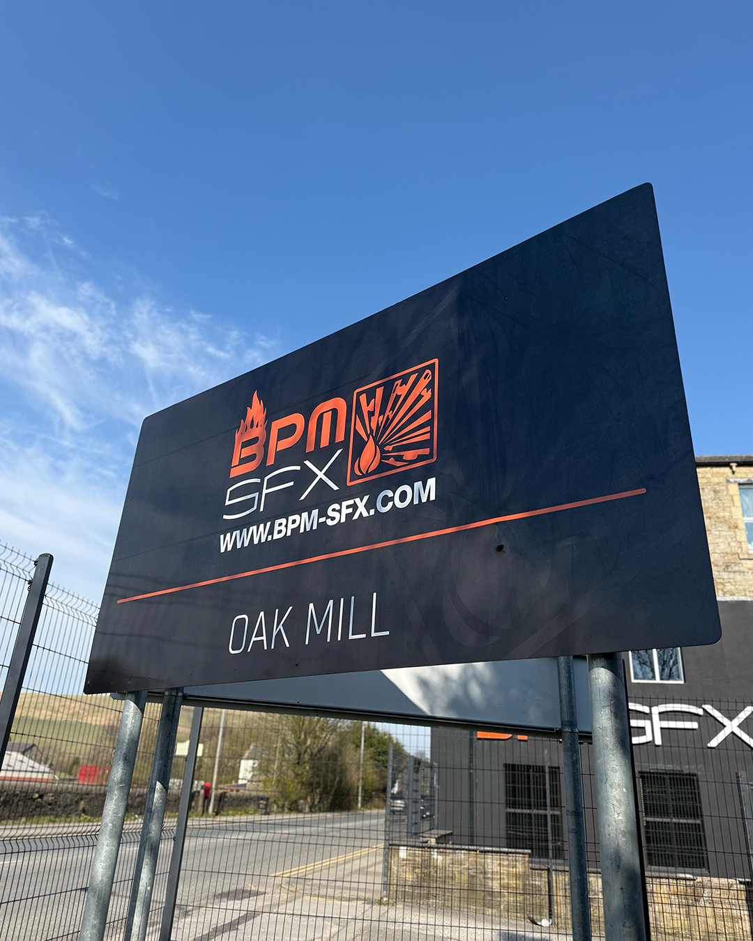 Outdoor sign for BPM SFX at Oak Mill, with blue sky and a building in the background.