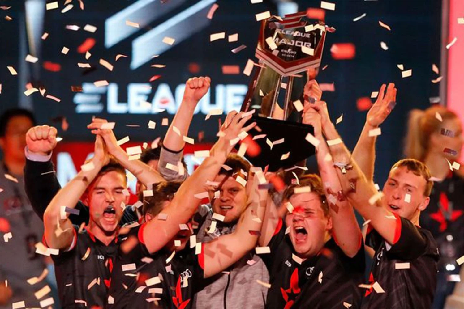 A group of esports team members celebrating victory as they lift a trophy amid falling confetti.