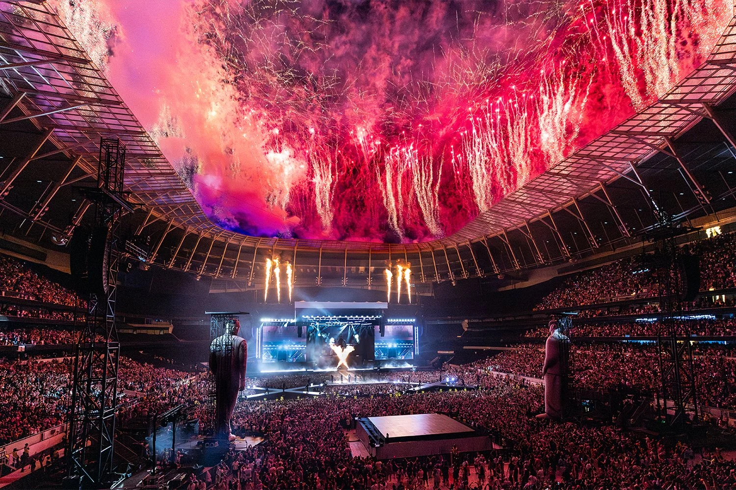 Crowd attending a large concert or music festival with a stage, fireworks, and laser lights in a stadium.