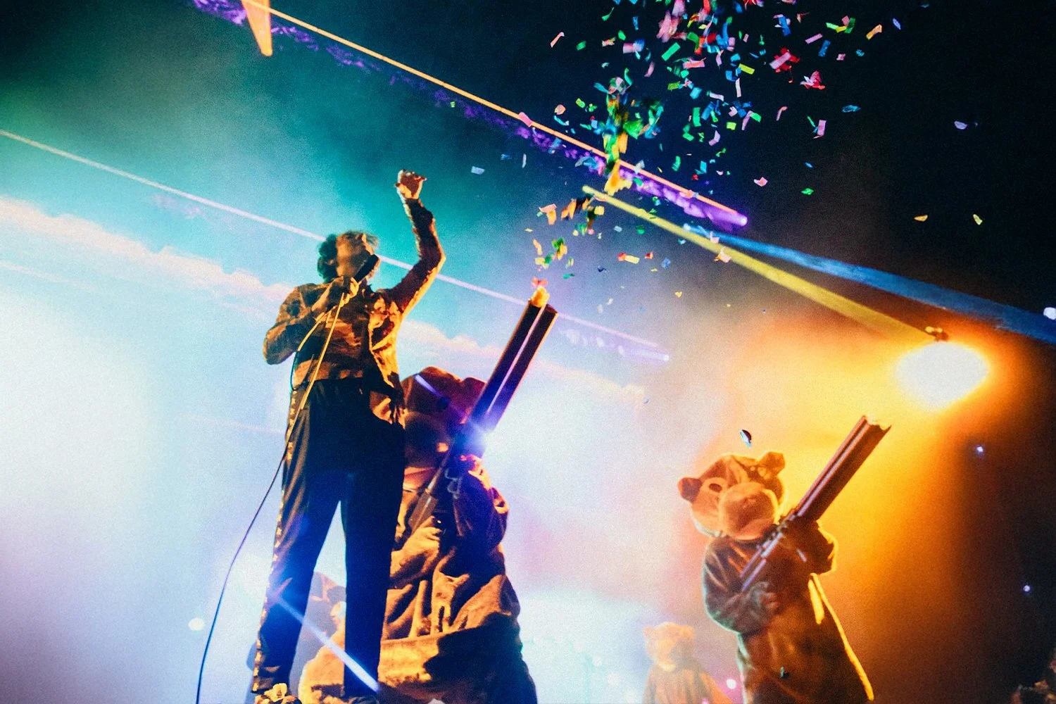People on stage celebrating with confetti, colorful lights, and a bright yellow spotlight.