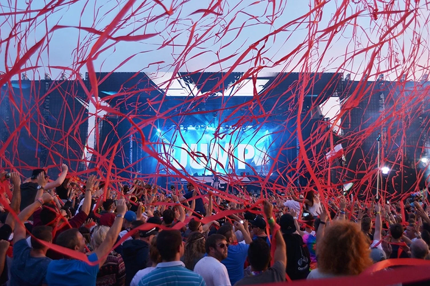 Crowd attending a concert with red streamers and blue stage lighting.