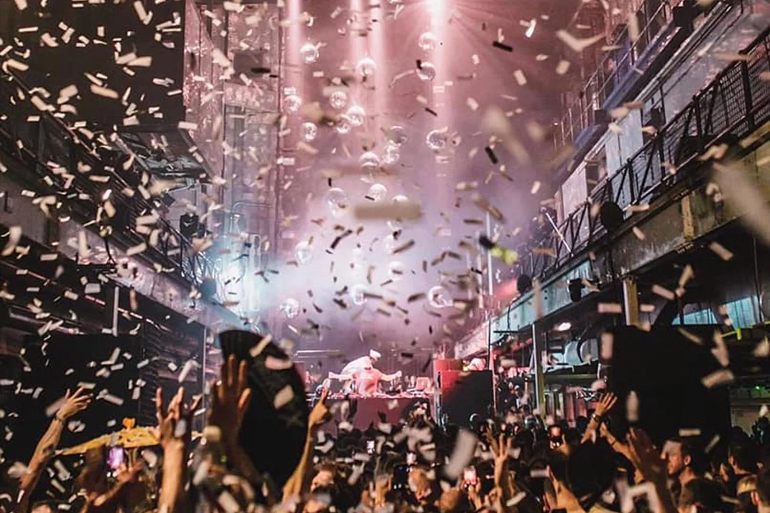 Crowd at a lively indoor concert with confetti falling and a DJ on stage.