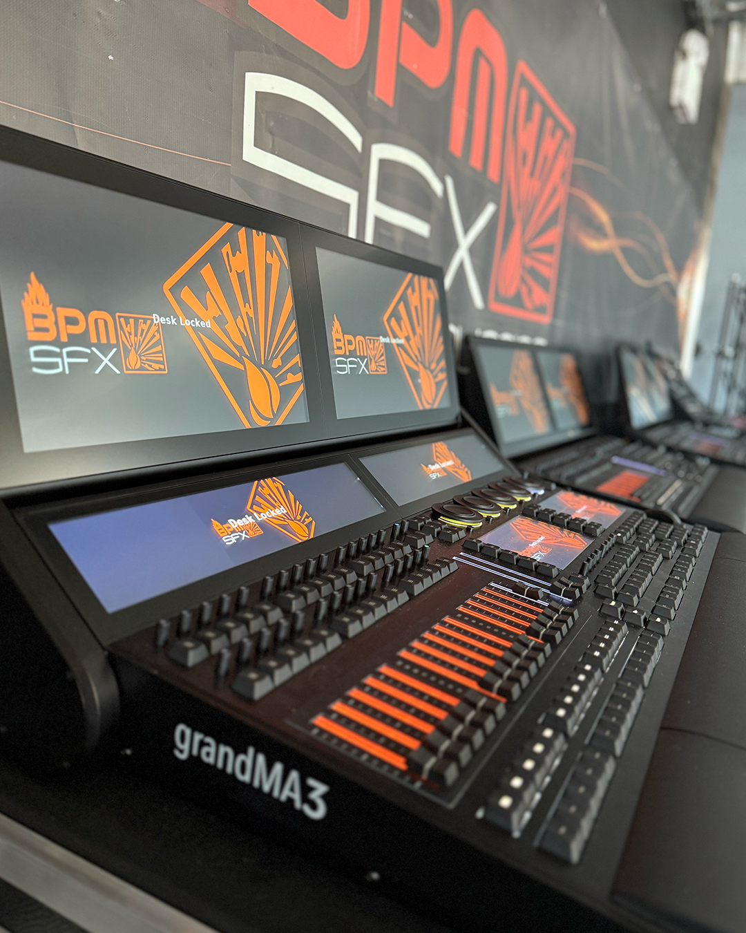 Multiple control consoles with screens displaying the logo and name 'BPM SFX' and the text 'Desk Locked,' set up at an event or studio, with a large banner in the background showing the same logo and name.