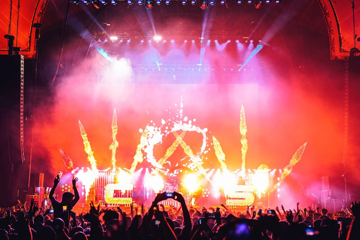 A concert with a large crowd, colorful lighting, and pyrotechnics on stage.