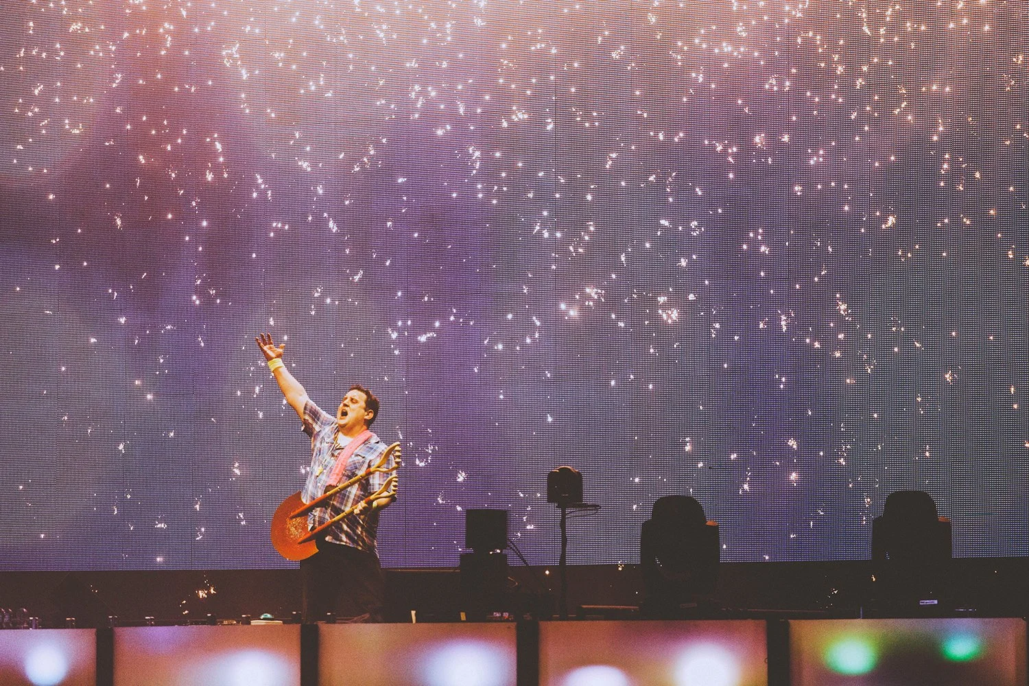 A DJ with a guitar on stage performs in front of a large digital screen displaying a starry sky and fireworks.