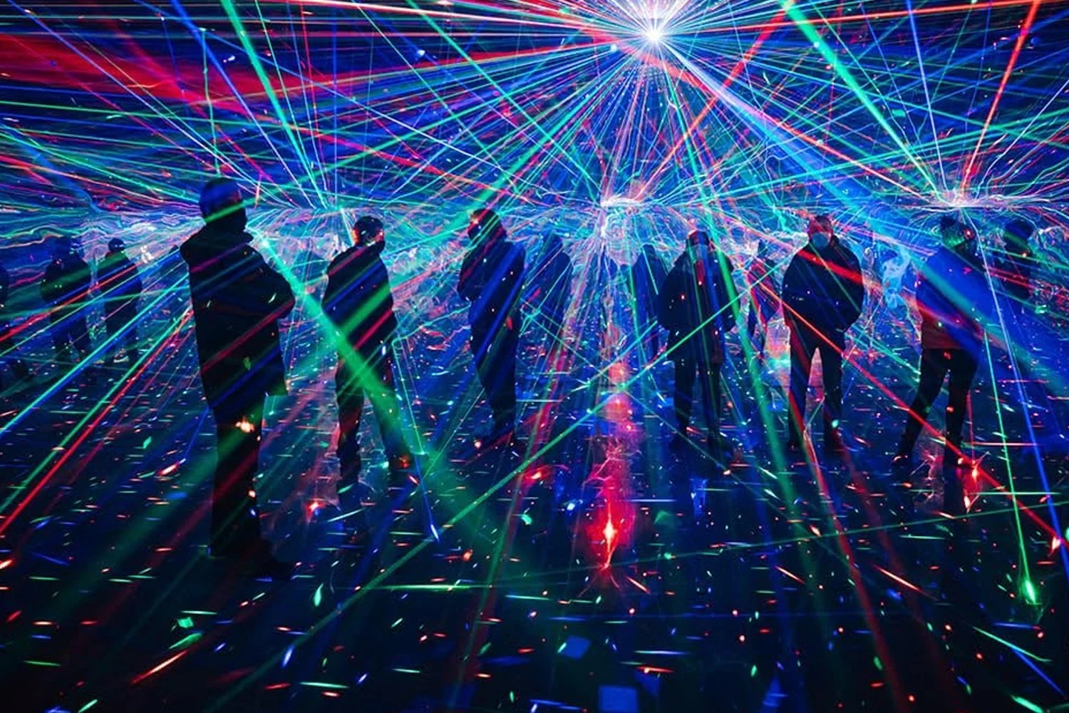 Silhouettes of people standing in a room filled with colorful laser light beams creating a futuristic, neon atmosphere.