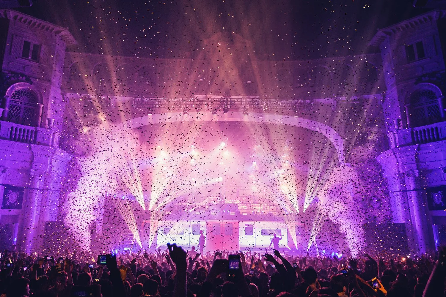 Concert or nightclub scene with purple and pink lighting, confetti falling, and a crowd with raised hands.