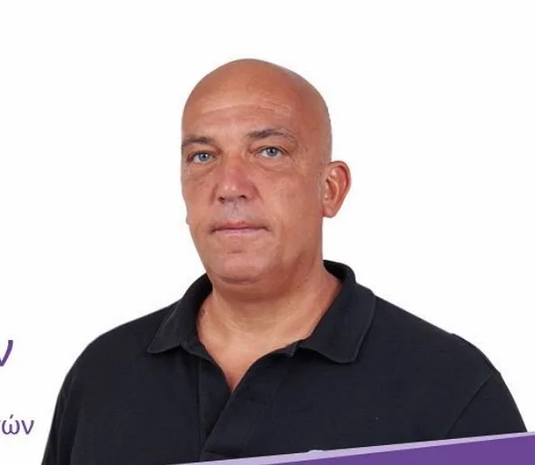 A bald man with light skin wearing a black collared shirt against a plain white background.