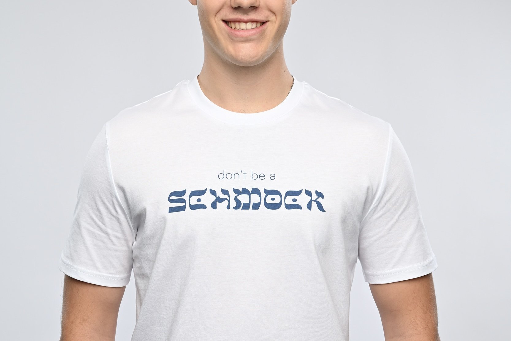 Ein junger Mann trägt ein weisses T-Shirt der Marke SHALOM.BERLIN mit blauem Aufdruck "don't be a SCHMOCK"