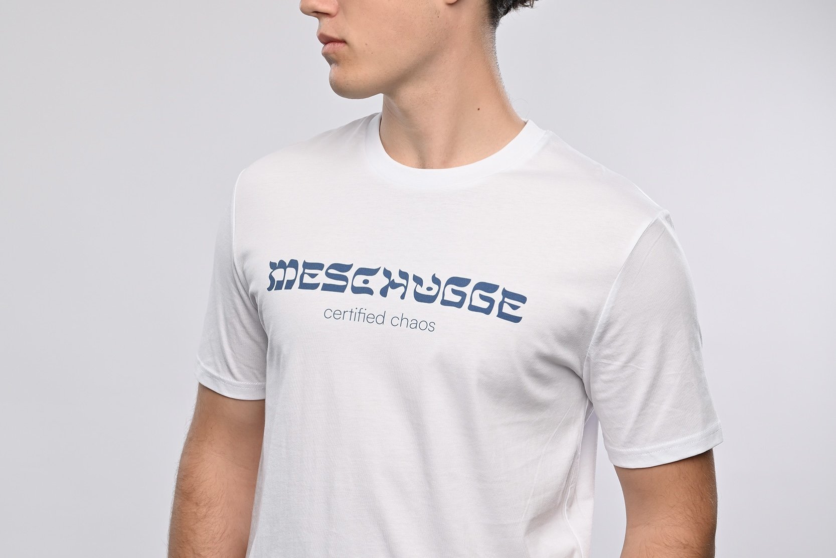 Ein junger Mann trägt ein weisses T-Shirt der Marke SHALOM.BERLIN mit blauem Aufdruck "MESCHUGGE certified chaos"